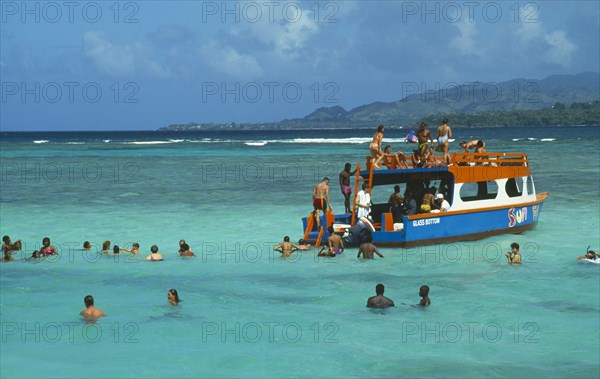 WEST INDIES, Tobago, Buccoo Reef, The Nylon Pool with tourists swimming or standing in shallow water by crowded glass bottom boat