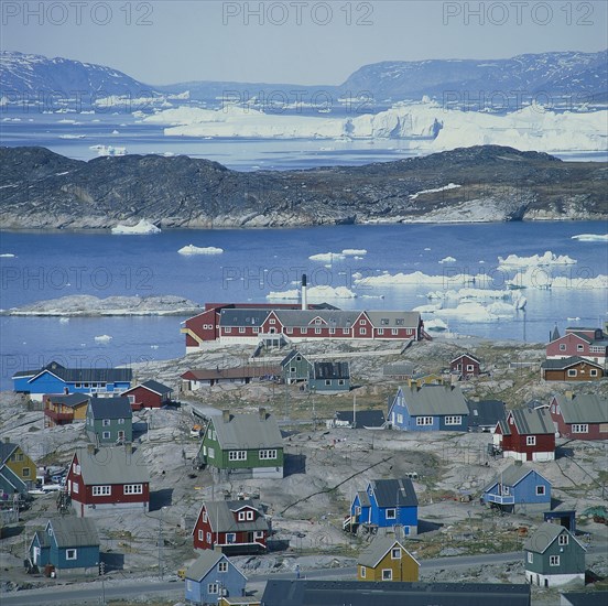 GREENLAND, Denmark, Jakobshaven, View over Ilulissat town with the sea and icebergs beyond coloured houses on rock