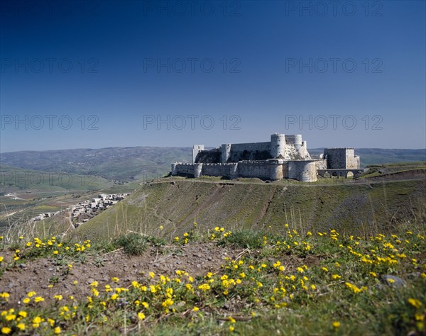 SYRIA, Central, Crac des Chevaliers, Crusader Castle in distance on plateau with village partly seen below