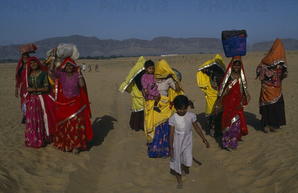 INDIA, Rajasthan, Pushkar, Brightly dressed Rajasthani women and children carrying loads on their heads.