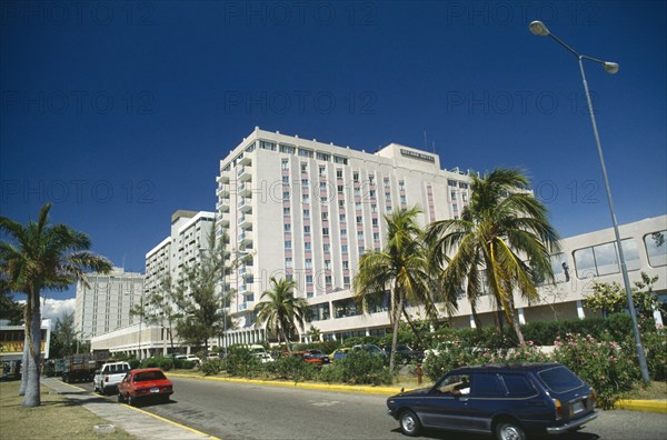 WEST INDIES, Jamaica  , Kingston, Downtown.  Oceana Hotel overlooking road lined by palm trees and parked cars.