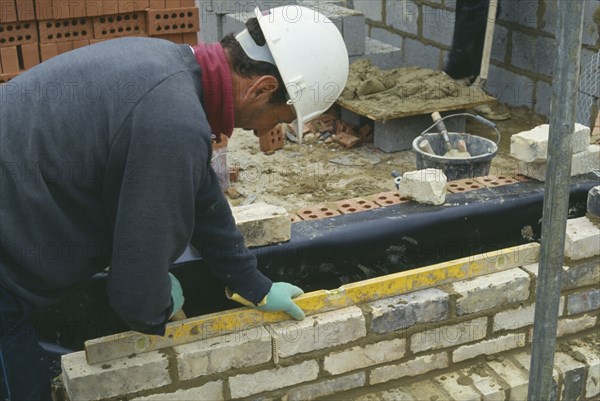 ARCHITECTURE, Construction, Bricklayer, Workman wearing a hard hat using a spirit level to lay reclaimed facing bricks