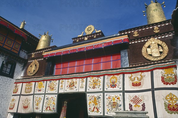 TIBET, Lhasa, Jokhang Temple, Golden Wheel of Dharma on roof of building covered in hanging fabrics with religious images