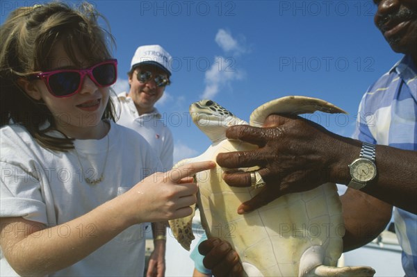 WEST INDIES, Cayman Islands, Grand Cayman, Young girl touching turtle held by man in the Turtle Farm