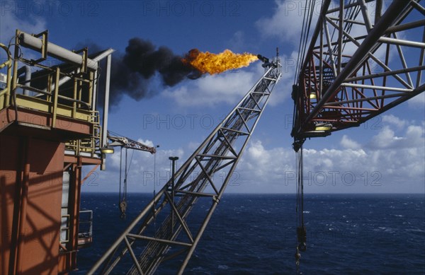 INDUSTRY, Factory, Oil Rig, Burning Off Gas. View along long pipe structure jutting out over the North sea to flames burning at the end