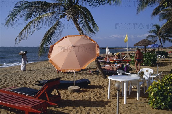 SRI LANKA, Negombo, Sandy beach with umbrella shading tourists lying on sunbeds and a shell vendor dressed in white