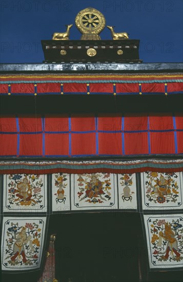 TIBET, Lhasa, Jokhang Temple, Golden Wheel of Dharma on roof of building covered in hanging fabrics with religious images