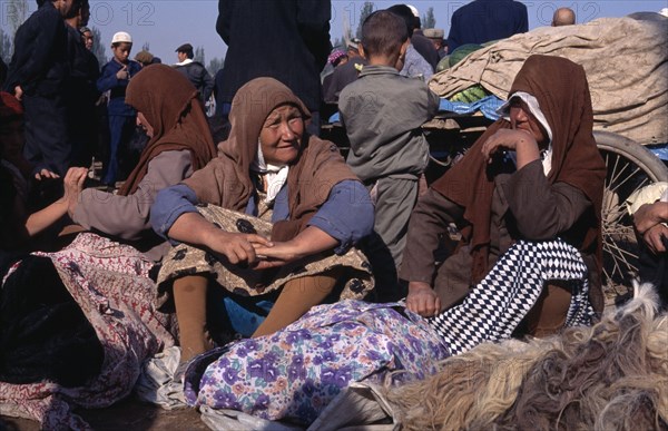 CHINA, Xinjiang, Kashgar, Women sitting with bundles of clothing at the Sunday Market