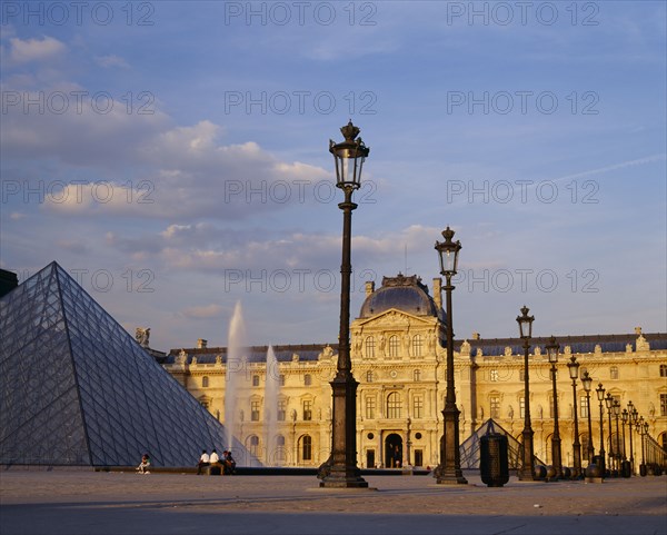 FRANCE, Ile de France, Paris, "Louvre,  Cour Napoleon and glass pyramid in evening light with decorative street lamps and fountain."