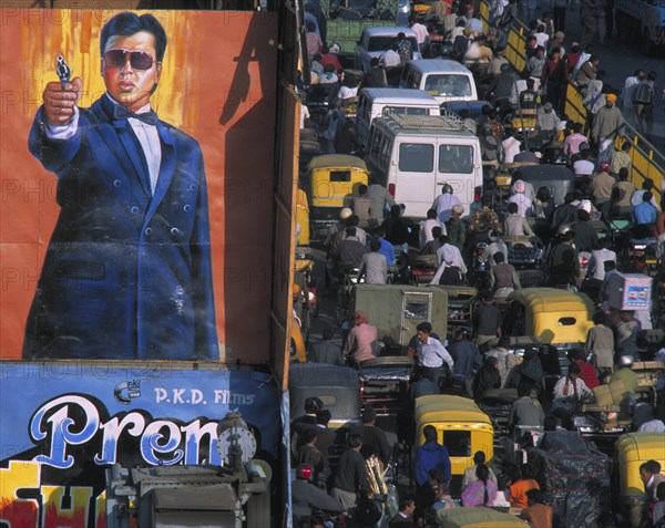 INDIA, Uttar Pradesh, Delhi, "Crowded street of Chandni Chowk with trucks, trishaws and people by cinema hoarding of man pointing a pistol"