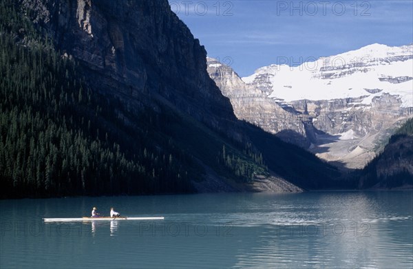 CANADA, Alberta, Banff National Park, Canoeist on Lake Louise with a backdrop of snow covered sheer cliffs and pine forests