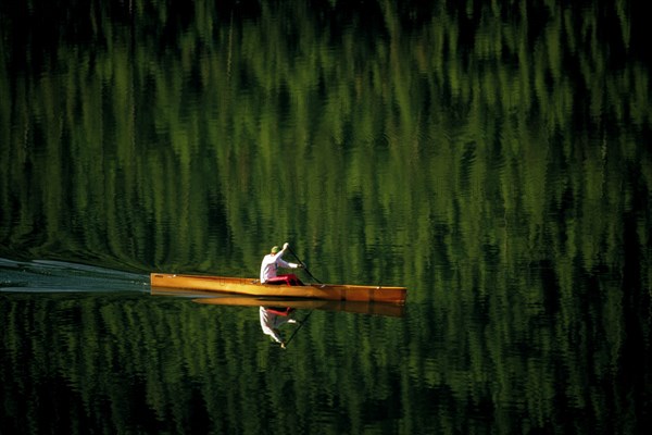 USA, Montana, Salmon Lake, Single canoeist on lake with reflection of trees in the water near Kalispell