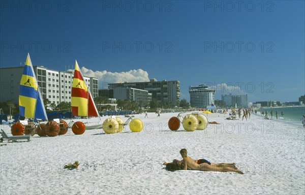 USA, Florida, St.Petersburg, "Sunbathers, Hobbie cats and pedalos on white sand beach with city buildings behind."