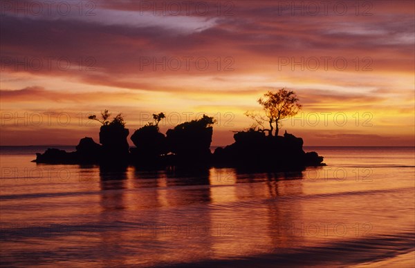 PHILIPPINES, Visayan Islands, Boracay Island, Rocky outcrop with trees just off shore silhouetted against dramatic sunset