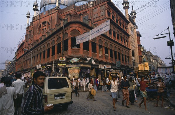 INDIA, West Bengal, Calcutta, "Nakhoda mosque built 1926.  Calcutta’s principal Muslim place of worship.  Red sandstone exterior with painted dome on busy street with people, traffic and shop fronts."