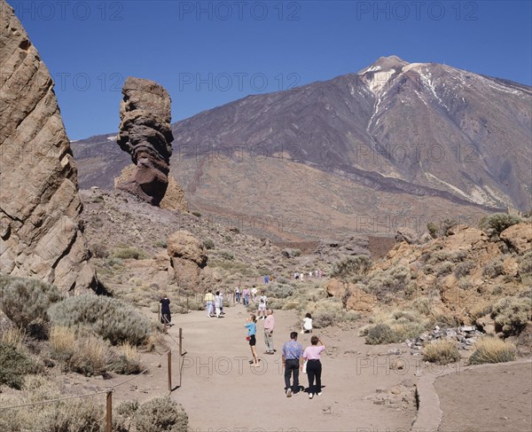 SPAIN, Canary Islands, Tenerife, Mount Teide National Park with tourists on dry and dusty path amongst rock formations with Teide in the distance
