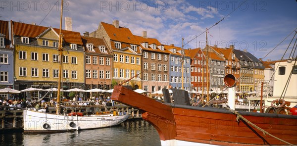 DENMARK,  , Copenhagen, Boats on Nyhavn Canal with pavement cafes and waterside buildings behind.