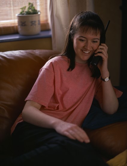 COMMUNICATIONS, Phones, Smiling teenage girl sat on sofa using cordless telephone Model Released ELT & Educational use only