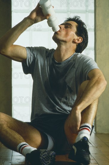 DRINK, Water, Man sat on ground infront of window drinking from a water bottle after workout