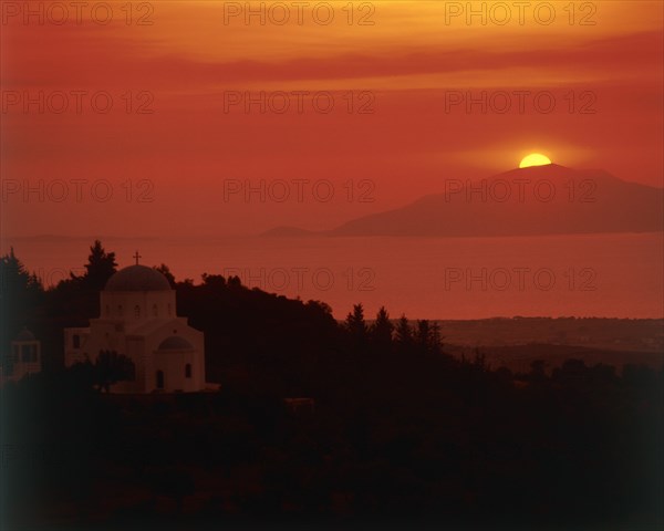 GREECE, Dodecanese Islands, Kos, "View past domed church in rural landscape to sun setting behind an island out at sea, view from Zia Taverna"