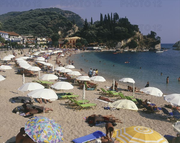 GREECE, Epirus Region, Parga, "Krioneri Beach, view along busy beach with umbrellas and sun loungers to rocky headland"
