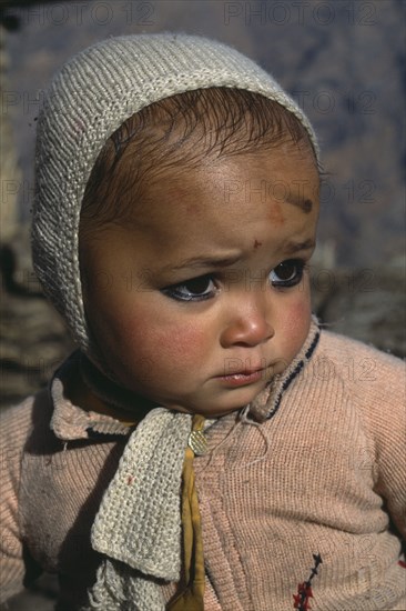 INDIA, Uttar Pradesh, Himalayan baby looking unhappy.  Black kohl ringed eyes and mark on forehead is thought to ward off the evil eye.