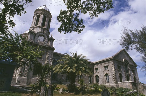 WEST INDIES, Antigua, St John’s, "Cathedral, exterior with clock tower and grave stones part framed by tree branches."