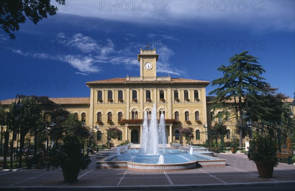 ITALY , Emilia Romagna, Cattolica, Elegant yellow town hall building with trees and a fountain in the foreground