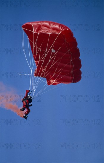 20003695 SPORT Air Parachuting Parachutist with red garments  red Parachute and with red smoke coming from his boots.