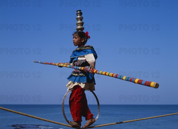 INDIA, Goa , General, "Young girl walks the tightrope while balancing silver pots on her head, blue sky in background"