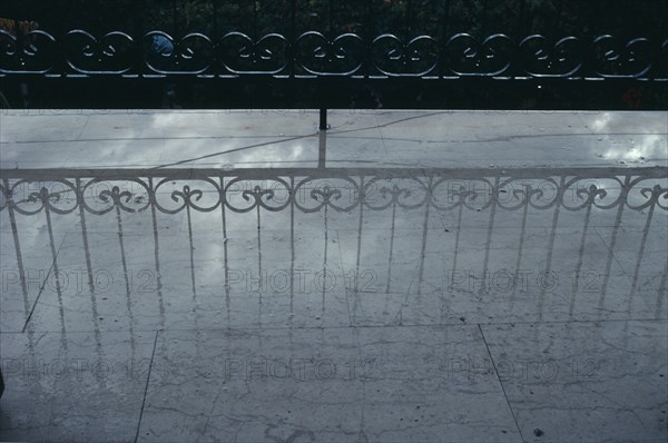 GREECE, Reflection, Decorative wrought iron balcony railings casting a shadow onto a pale wet floor.
