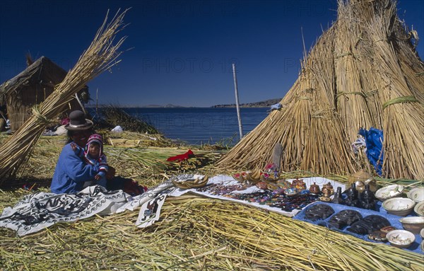 PERU, Puno Administrative Divsion, Lake Titicaca , "Woman and child seated outside a reed house on a floating island, decorative wares displayed beside them. "
