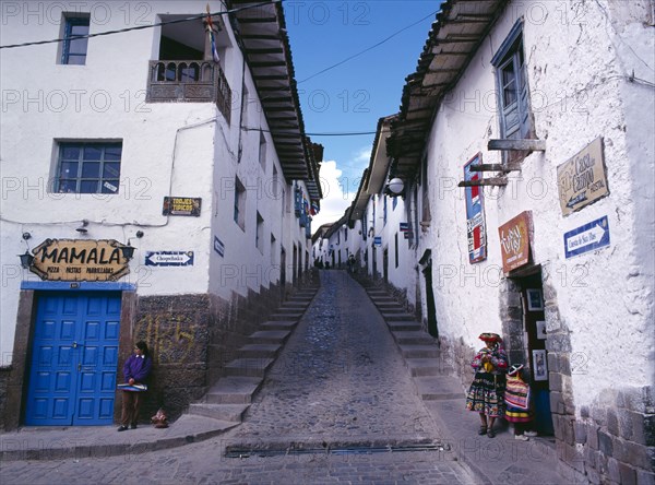 PERU, Cusco Department, Cusco, View up a narrow street between white painted houses.   Woman and child in peasant dress standing opposite a woman in modern dress at the bottom.
