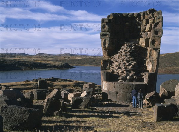 PERU, Puno Administrative Division, Puno Area, "Sillustani.  Pre columbian funeral tower, or chullpa, with two people standing at it´s base, looking upwards.  "