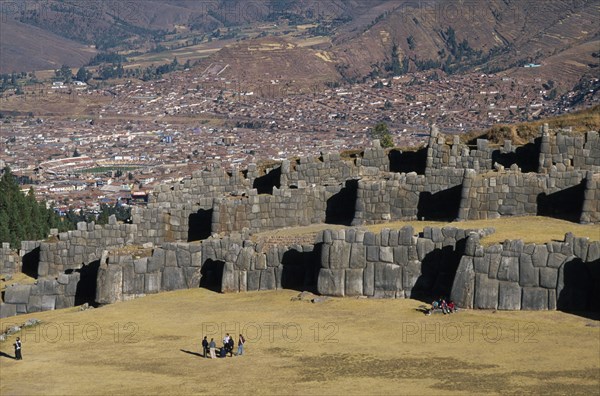 PERU, Cusco Department, Sacsayhuamán, Looking down on visitors walking between the Inca walls and Cusco in the distance.