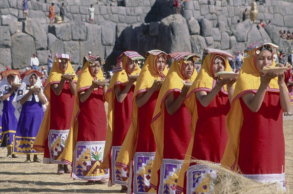 PERU, Cusco Department, Sacsayhuaman, Parade of women offering  food at Inti Raymi.  Inca walls behind.