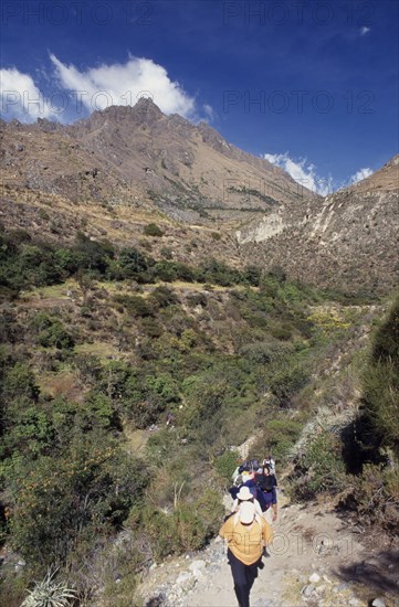 PERU, Cusco Department, The Inca Trail, "Treckers with back packs walking up a narrow pathway, mountains behind them."