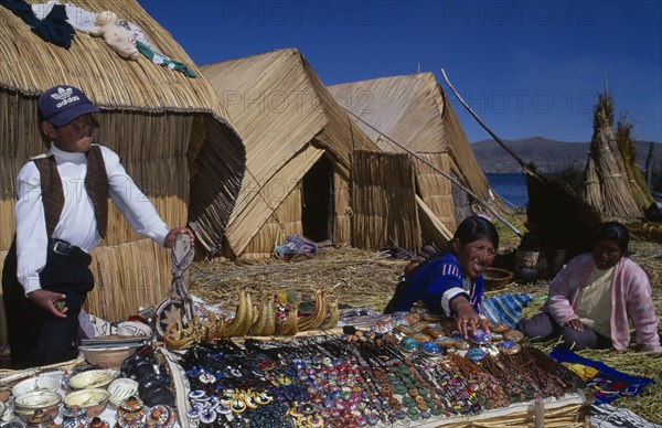 PERU, Puno, Lake Titicaca, Uros women and young boy selling sounvenirs outside reed houses on a floating island.