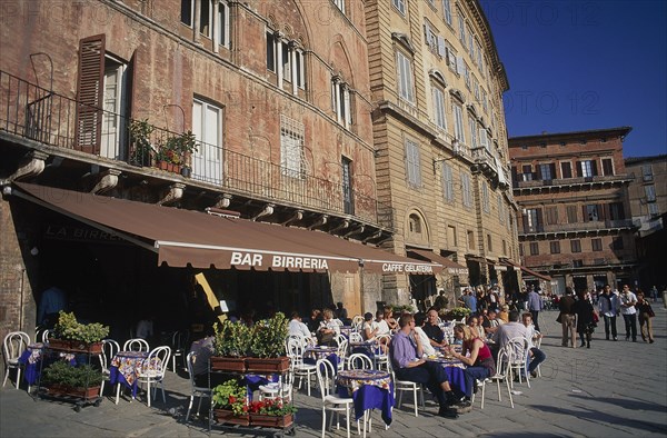 ITALY, Tuscany, Sienna, The Piazza del Campo with people sitting at tables under umbrellas outside a restaurant