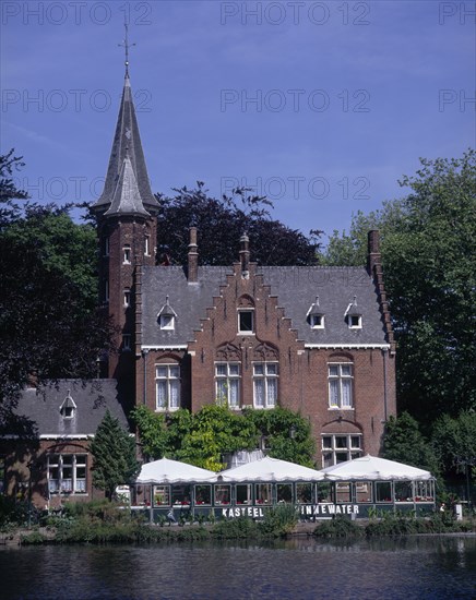 BELGIUM, West Flanders, Bruges, "View across Minnewater or Love Lake, towards red brick building with tiled, turreted roof with gabled windows."