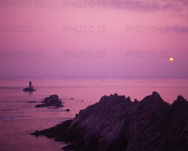 FRANCE, Brittany, Finistere, "Near Audierne.  Pointe du Raz at sunset.  Rocks silhouetted against a purple sky, reflected in the water."