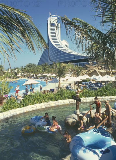UNITED ARAB EMIRATES, Dubai, "View over Wild Wadi water park pools, people in the water with inflatable rings in the foreground. Chicago Beach Hotel behind.  "