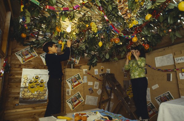 SOCIETY, Religion, Judaism, England.  Jewish children decorating the ceiling of a Sukka with cut branches and fruit during the Sukkot Festival.