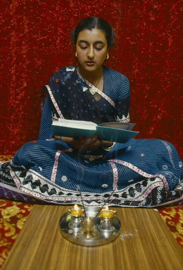 SOCIETY, Religion, Hinduism, England.  Girl reading Holy book in front of lighted candles and incense during Dirwali.