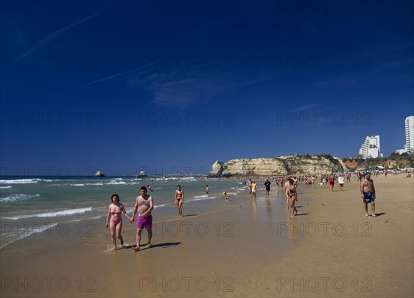 PORTUGAL, Algarve, Praia da Rocha, View along beach with people walking along the waters edge