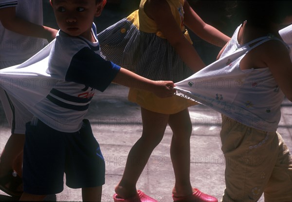 VIETNAM, Hanoi, "Group of young children, holding on to each other’s clothing to form a line. "