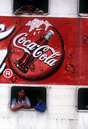 VIETNAM, Mekong Delta, Vinh Long, "Advertisment for Coca Cola on the side of a ferry, passengers at the windows above and below it."