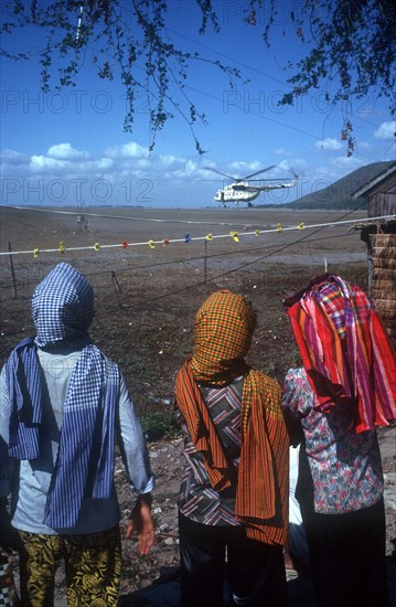 CAMBODIA, Tinh Bien, Three figures in the foreground watching a UN helicopter on the Vietnamese border.