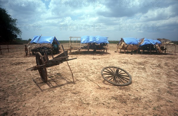 CAMBODIA, Kompong Thom, "Phnom Prasat refugee camp on national Route 6, people just visible in makeshift huts with a broken cart in the foreground."