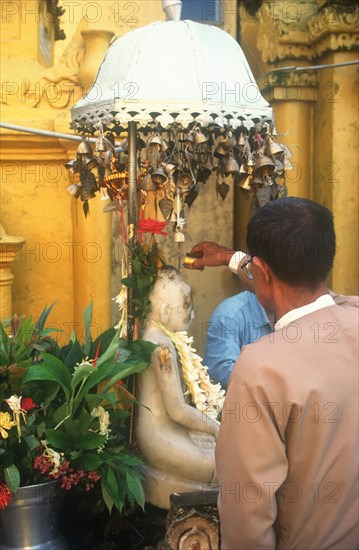 MYANMAR, Yangon, Shwedagon Pagoda. Man making offering at temple shrine.